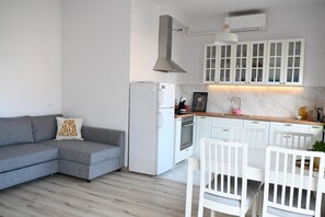 A modern kitchen with white cabinets, a built-in oven, and a grey sofa.