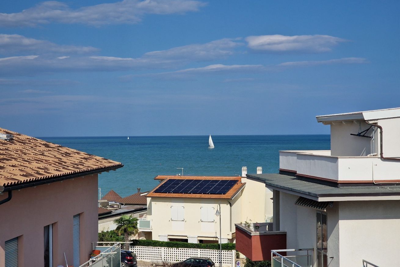 Una zona residenziale sul lungomare con vista sul mare, un'imbarcazione a vela e edifici dotati di pannelli solari.