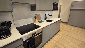 A modern kitchen with a black stove, a sink, and a microwave. There is a wooden cutting board and a knife block on the counter.