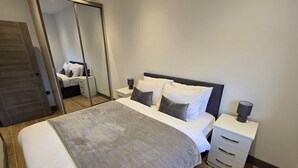 A modern bedroom with a large bed, a nightstand, a mirror, and a wardrobe.