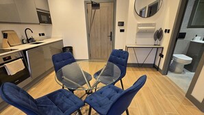 A modern kitchen with a round glass table and four blue chairs, a wooden door, and a mirror on the wall.