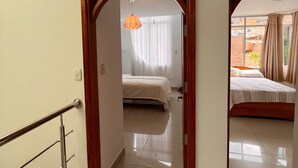 Een hotelkamer met een bed, een raam met gordijnen en een gang naar een andere kamer.