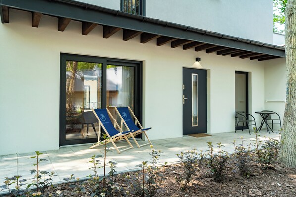 A modern building with a covered patio area, a door, and two lounge chairs. - Baltic Forest (Kolobrzeg)