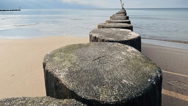 Egy fahíd vezet egy felhős égbolt alatt fekvő strandhoz.