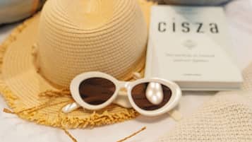 Un lit avec un couvre-lit blanc texturé, sur lequel on aperçoit un chapeau beige, des lunettes de soleil, un livre intitulé « cisza » et une petite figurine.
