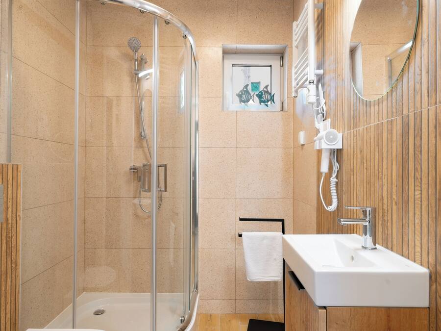 Ein modernes Badezimmer mit einer gläsernen Duschkabine, einem weißen Waschbecken und einer Holz-Kommode.