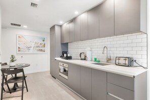 Una cocina moderna con gabinetes grises, encimera blanca, un lavamanos, un tostador y una cafetera.