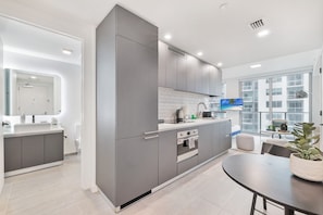 Una cocina moderna con armarios grises, encimera blanca y un amplio ventanal con vistas a la ciudad.