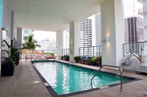 An indoor swimming pool with lounge chairs and potted plants, surrounded by tall buildings. - Chic Downtown Studio With Rooftop Pool and Gym (Miami)