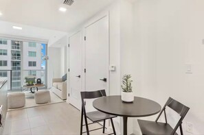 Una habitación moderna y bien iluminada con una mesa redonda y cuatro sillas, una planta en maceta y vistas a un balcón con un sofá y una mesa.