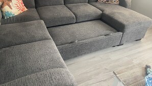 Un canapé d’angle gris avec une méridienne, deux coussins décoratifs et un plancher en bois.