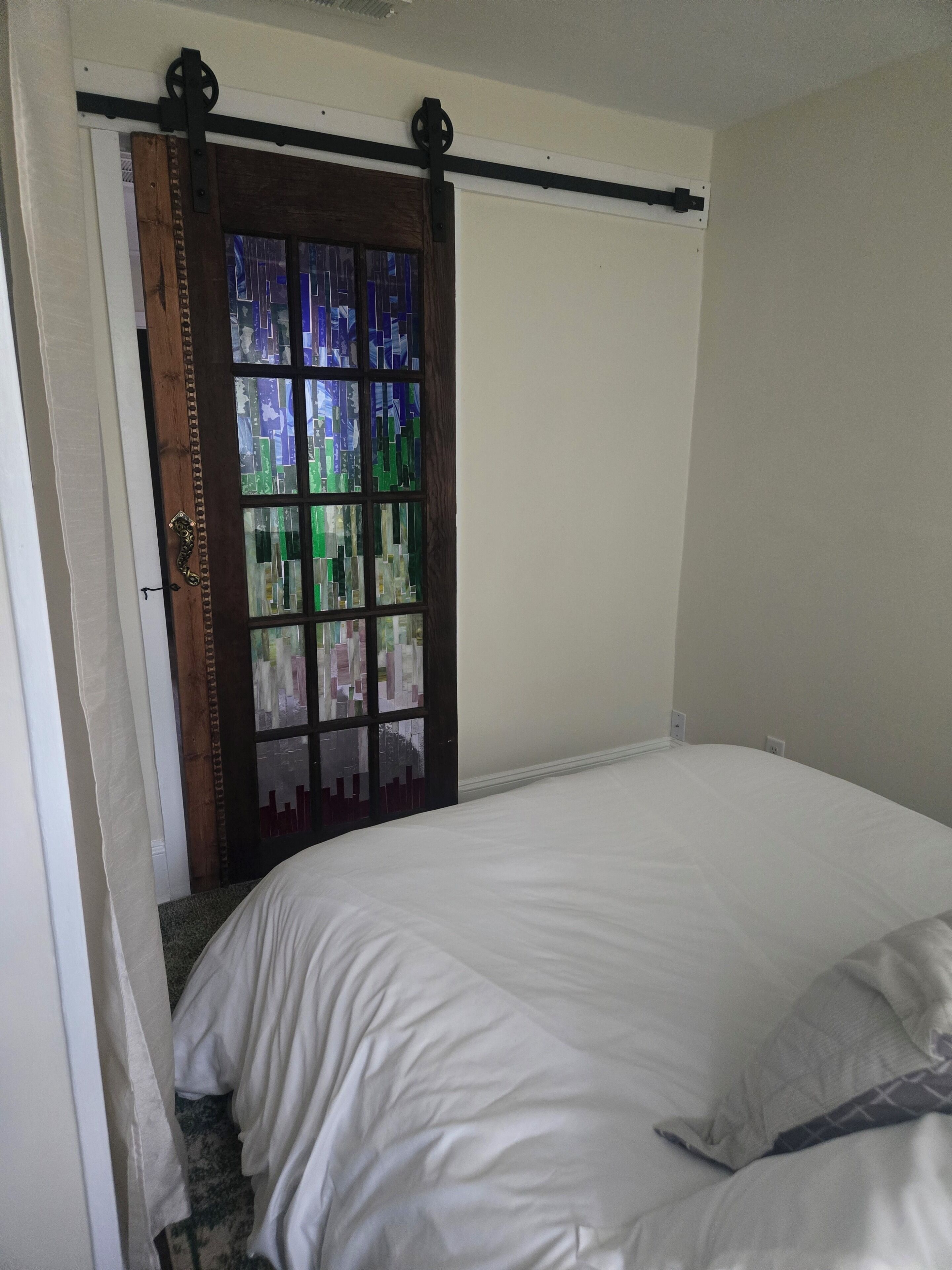 Een slaapkamer met een bed, een raam met glas-in-lood en een deur met houten frame.
