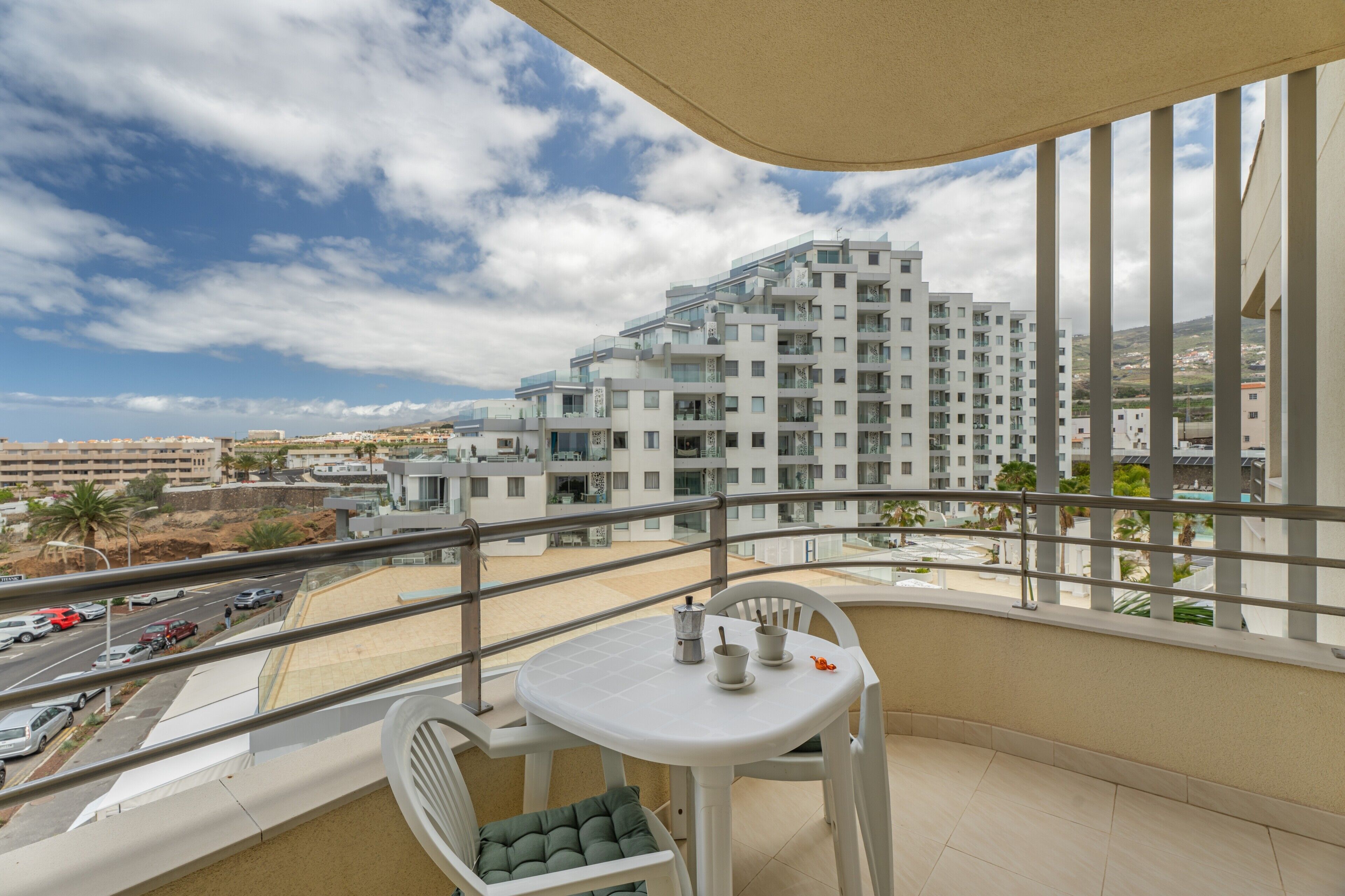 Un balcon avec une table et des chaises, donnant sur une rue et des immeubles modernes.