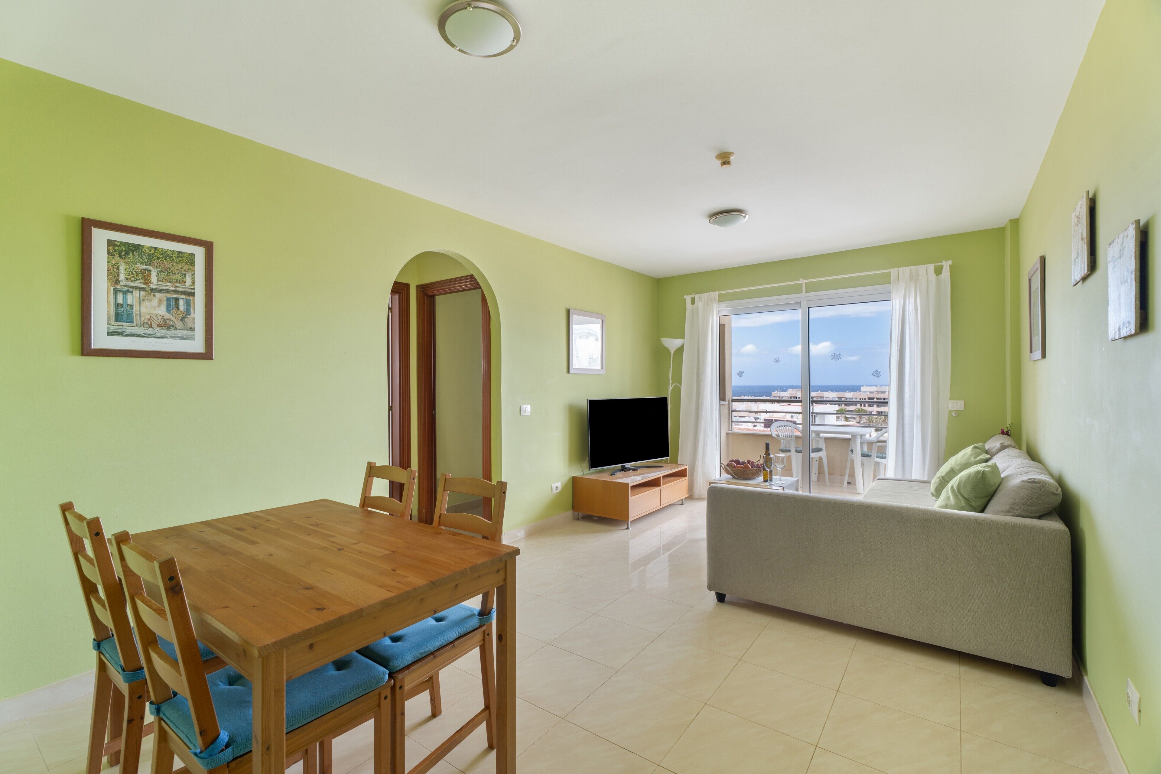 Una sala de estar con una mesa de comedor, sofá, televisor y un balcón con vistas.