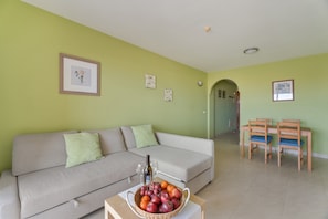 Una sala de estar con un sofá, una mesa de comedor con sillas y un frutero sobre la mesa.