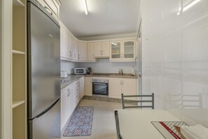 Una cocina compacta con armarios blancos, un refrigerador de acero inoxidable, un microondas y un horno.