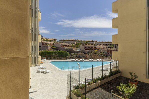 A rooftop pool with lounge chairs, a fenced area, and a view of other buildings.
