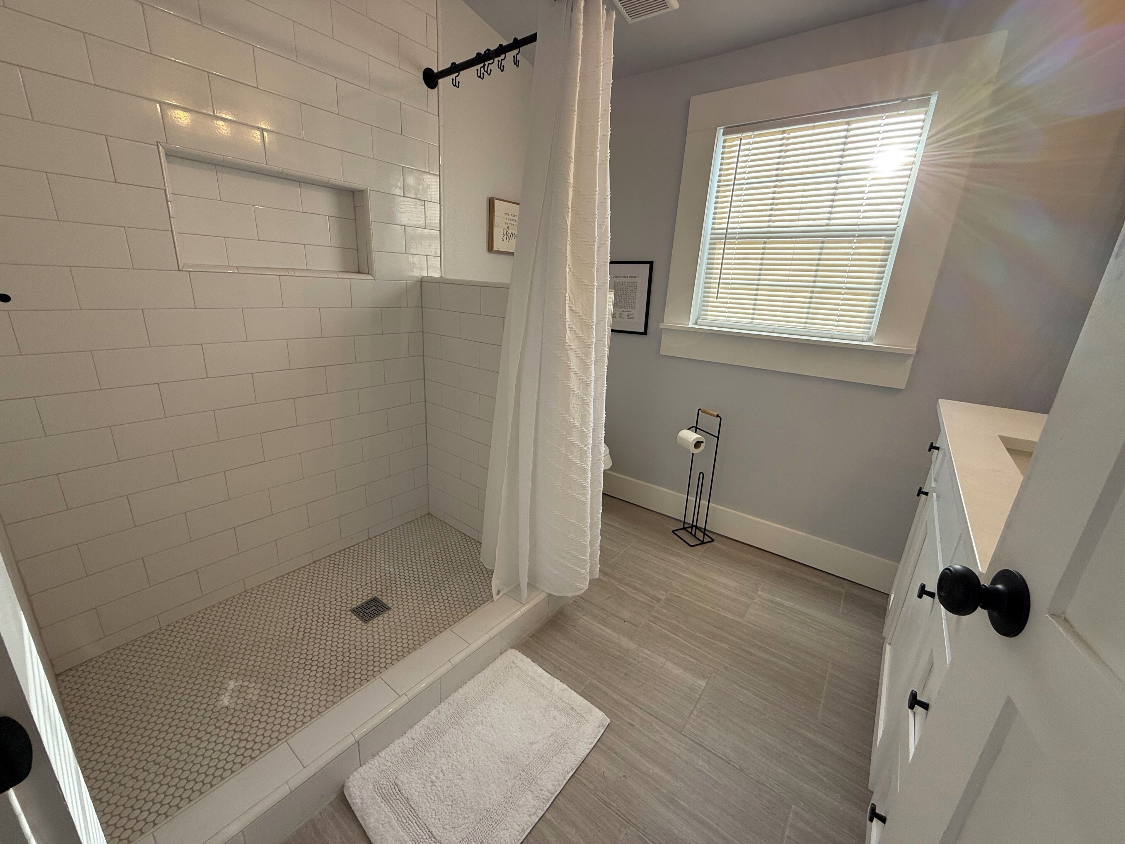 Une salle de bain moderne équipée d’une douche, d’un porte-rouleau de papier toilette et d’une fenêtre avec des stores.