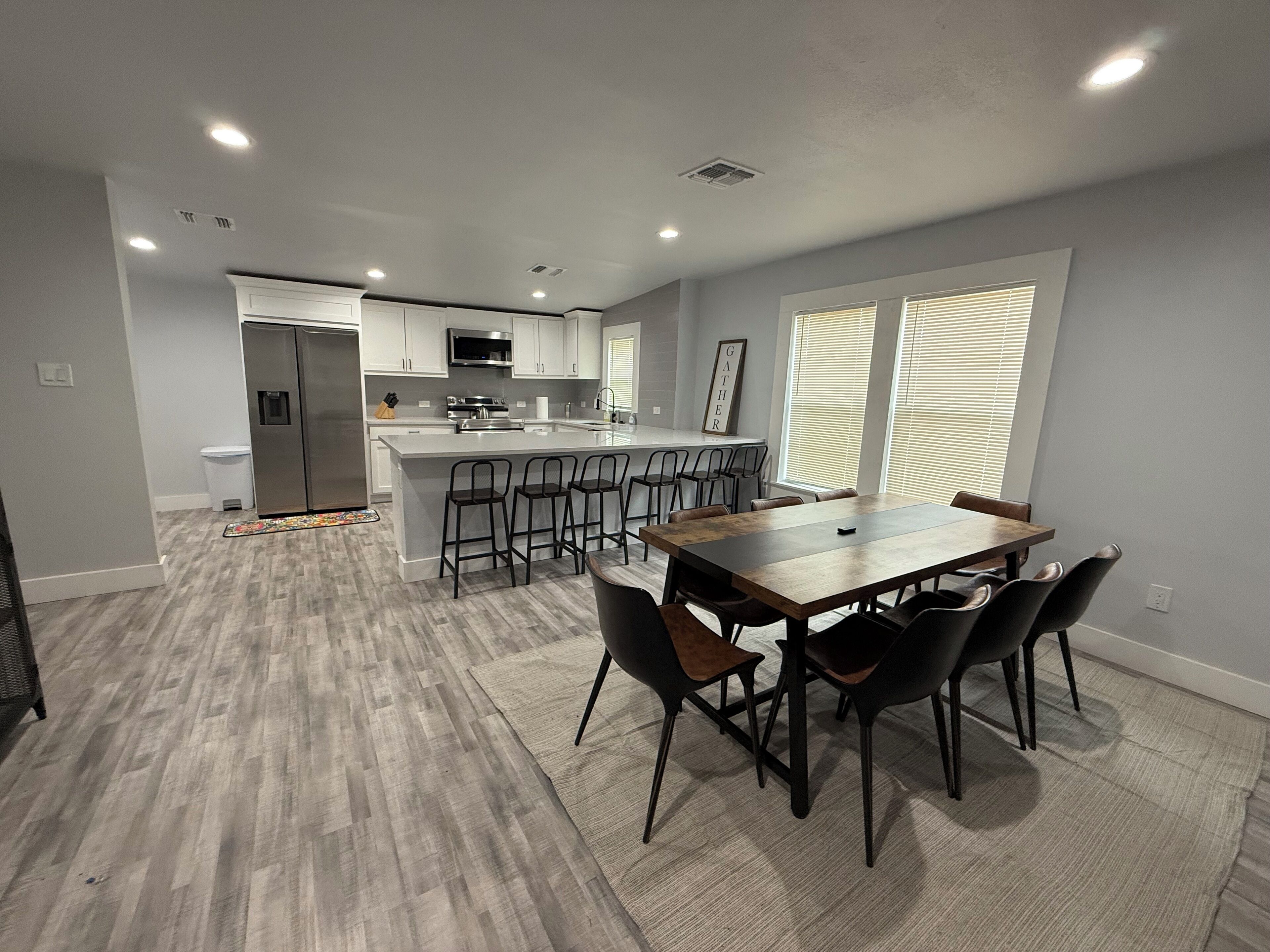 A modern kitchen with a central island, bar stools, and a dining table with chairs.