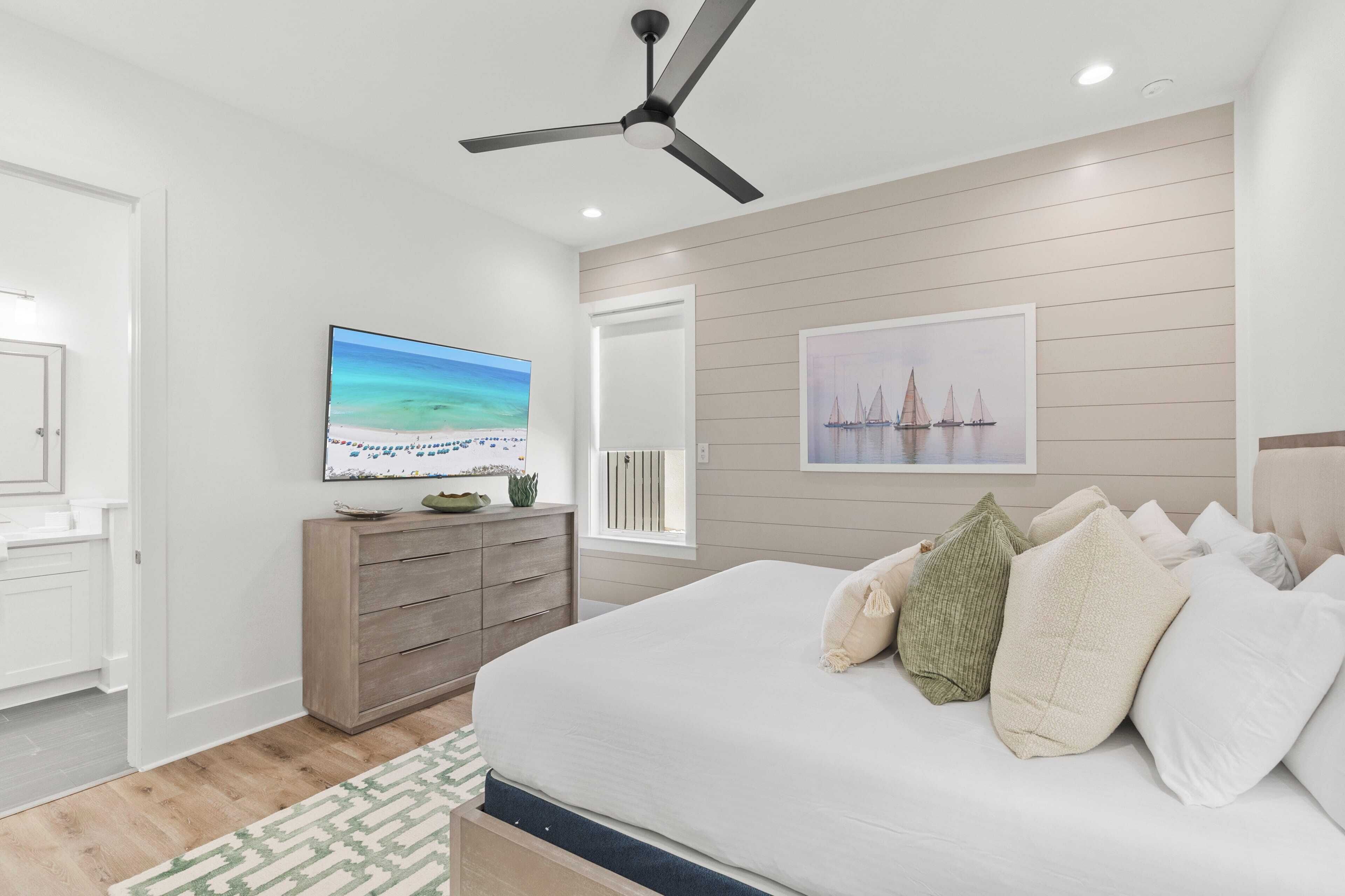 A bedroom with a bed, a ceiling fan, a TV, and artwork on the wall.