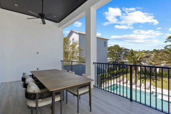 A balcony with a wooden table and chairs, a pool, and a view of neighboring houses.