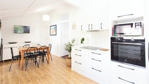 Et moderne køkken med hvide skabe, en indbygget ovn og et spiseområde med et træbord og stole.