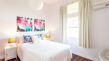 A bedroom with a bed, two bedside tables with lamps, a wall-mounted air conditioner, and a window with curtains.