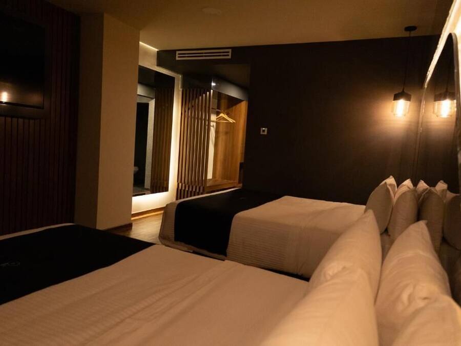 Quarto de hotel com duas camas, uma televisão presa à parede e um candeeiro suspenso.