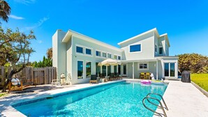 Una casa moderna de dos pisos con piscina, mobiliario exterior y un patio cubierto.