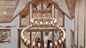 A spacious interior with a large wooden ceiling, a central chandelier, and multiple windows offering views of the outdoors.