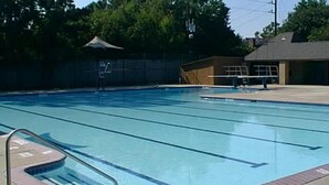 Ein Schwimmbecken mit Bahnen, einem Sprungturm und einem überdachten Sitzbereich.