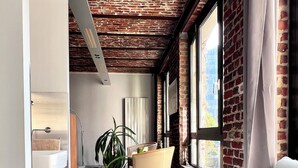 Ein modernes Interieur mit Backsteinwand, großen Fenstern, einer Couch, einem Tisch und einer Pflanze.