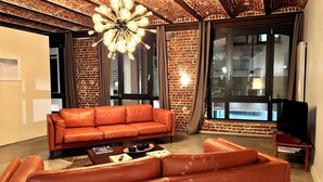 Ein modernes Wohnzimmer mit einer Ziegelwand, einem Ledersofa, einem Couchtisch und einem großen Fenster mit Vorhängen.