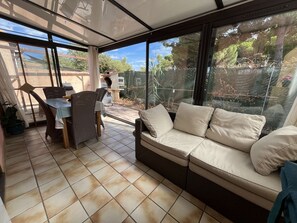 A sunlit patio with a cushioned seating area, a table, and chairs.