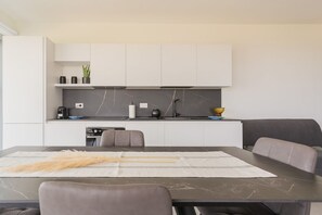 A modern kitchen with white cabinets, a marble backsplash, and a dining area with a table and chairs.