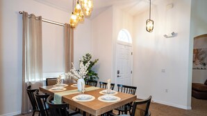 A dining room with a wooden table set for four, surrounded by black chairs, a vase with flowers, and a chandelier. - 2 King 2 Twin 1 Queen + Enormous Deck 3 BD Lakeview by Waterfront Park & Events (Clermont)