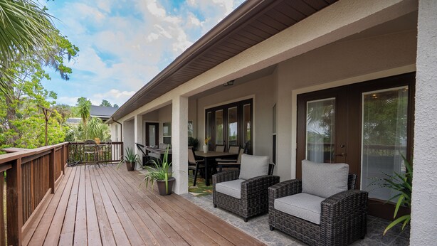 A covered outdoor patio with wicker furniture and a wooden deck. - 2 King 2 Twin 1 Queen + Enormous Deck 3 BD Lakeview by Waterfront Park & Events (Clermont)