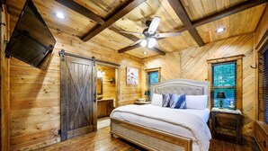 A wooden cabin bedroom with a bed, a ceiling fan, a nightstand, and a window with blinds.