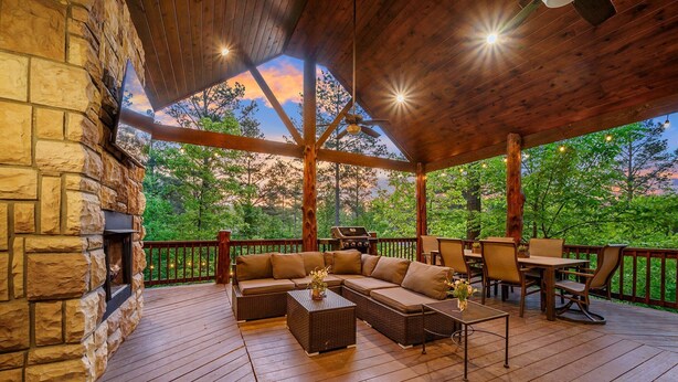 A covered outdoor deck with stone walls, a wooden ceiling, and a view of trees.