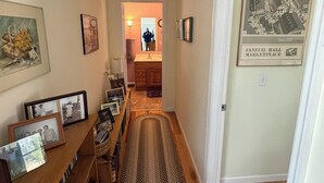 A hallway with a wooden bench, framed photos, a rug, and a vintage market place poster.