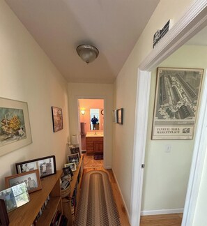 A hallway with a wooden bench, framed photos, a rug, and a vintage market place poster.