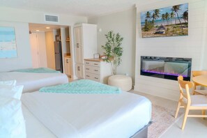 Habitación de hotel con dos camas, zona de comedor, chimenea y un cuadro con motivos playeros.