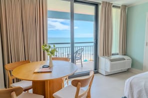 Camera d'albergo con balcone, tavolo da pranzo, sedie, una pianta e condizionatore.