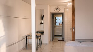 A hotel room with a bed, a small desk, and a chair. There is a kitchen area with a sink and a mirror.