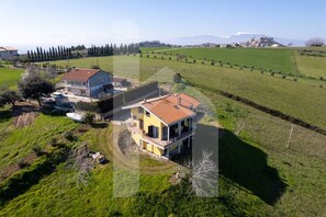A two-story house with a red roof, surrounded by green fields and a mountain in the background. - Homiday - Villa Moretti (Colonnella)