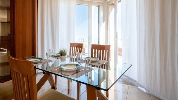 A dining area with a glass table, wooden chairs, and a view of the outdoors. - Homiday - Villa Moretti (Colonnella)