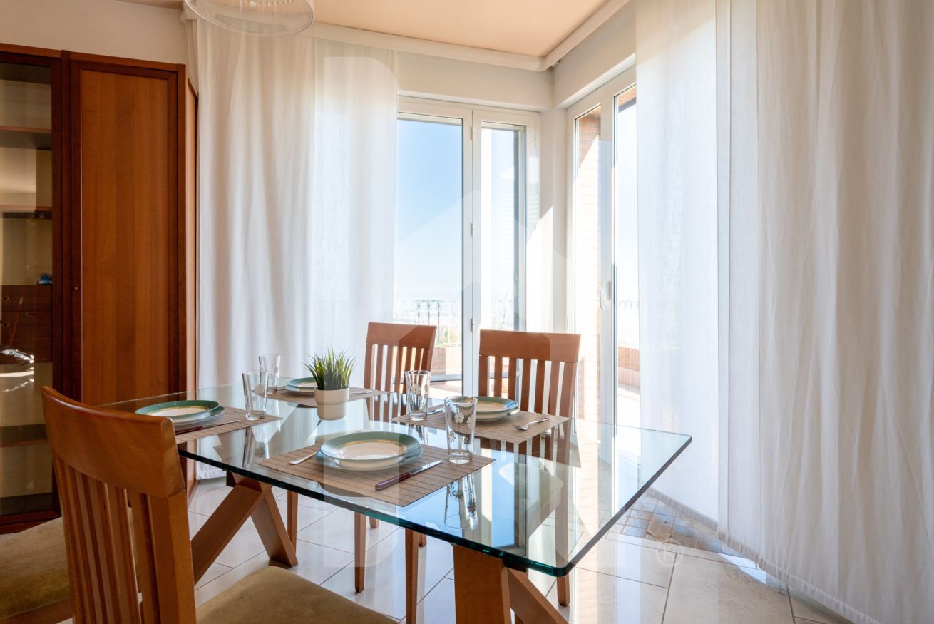 A dining area with a glass table, wooden chairs, and a view of the outdoors.