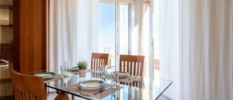 A dining area with a glass table, wooden chairs, and a view of the outdoors.
