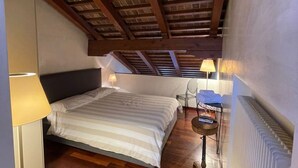 Une chambre avec un plafond en pente, un lit avec une literie à rayures, deux lampes de chevet, une chaise et une petite table sur laquelle se trouve un livre.