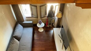 Un espace de vie compact comprenant un canapé, une petite table ronde et une lampe. Il y a une fenêtre avec des rideaux et une vue sur l’extérieur.